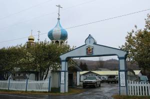 An arch marks the entrance to the Church of St. Nicholas on Tuesday, Oct. 10, 2023, in Nikolaevsk, Alaska. In rear, cars are parked in front of a building that has been used this school year as a makeshift classroom for families part of a home-school cooperative. (Ashlyn OHara/Peninsula Clarion)