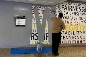 A worker paints over a wall mural featuring words such as fairness, leadership, compassion, diversity and integrity at the FBI Academy at Quantico on Wednesday. (Anonymous photo provided to The New York Times)