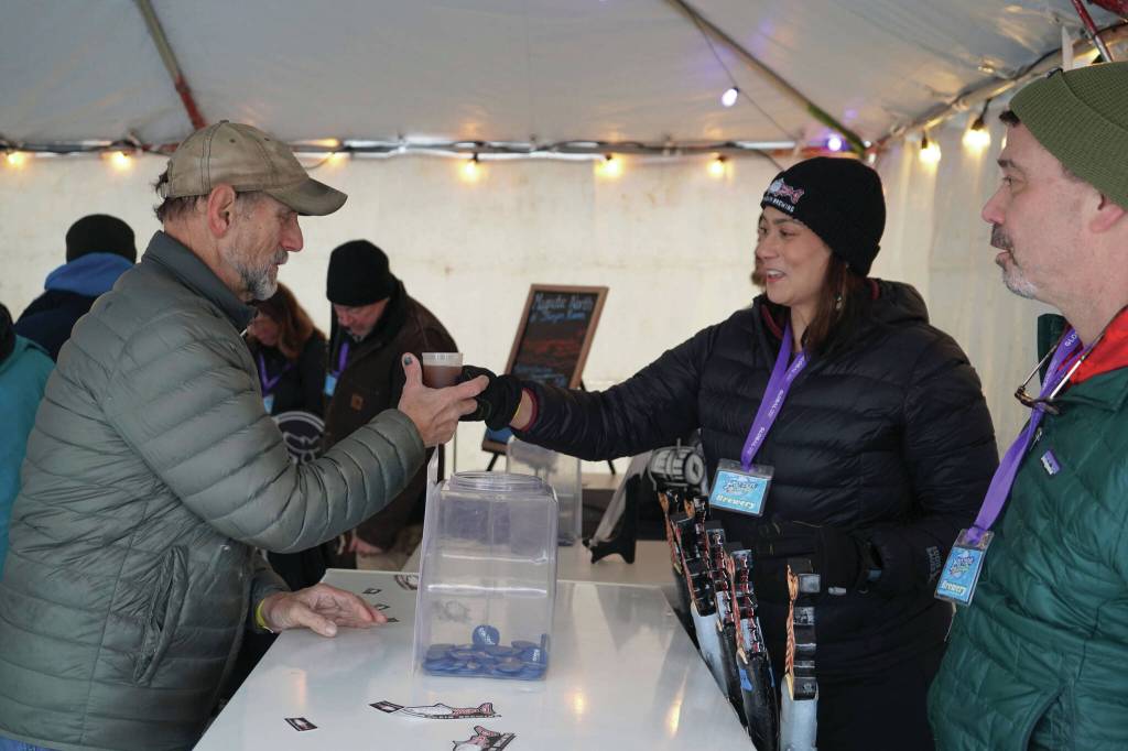 Brewers from Turnagain Brewery hand a freshly filled cup to an attendee at the 10th Annual Frozen River Fest in Soldotna, Alaska, on Saturday, Feb. 15, 2025. (Jake Dye/Peninsula Clarion)