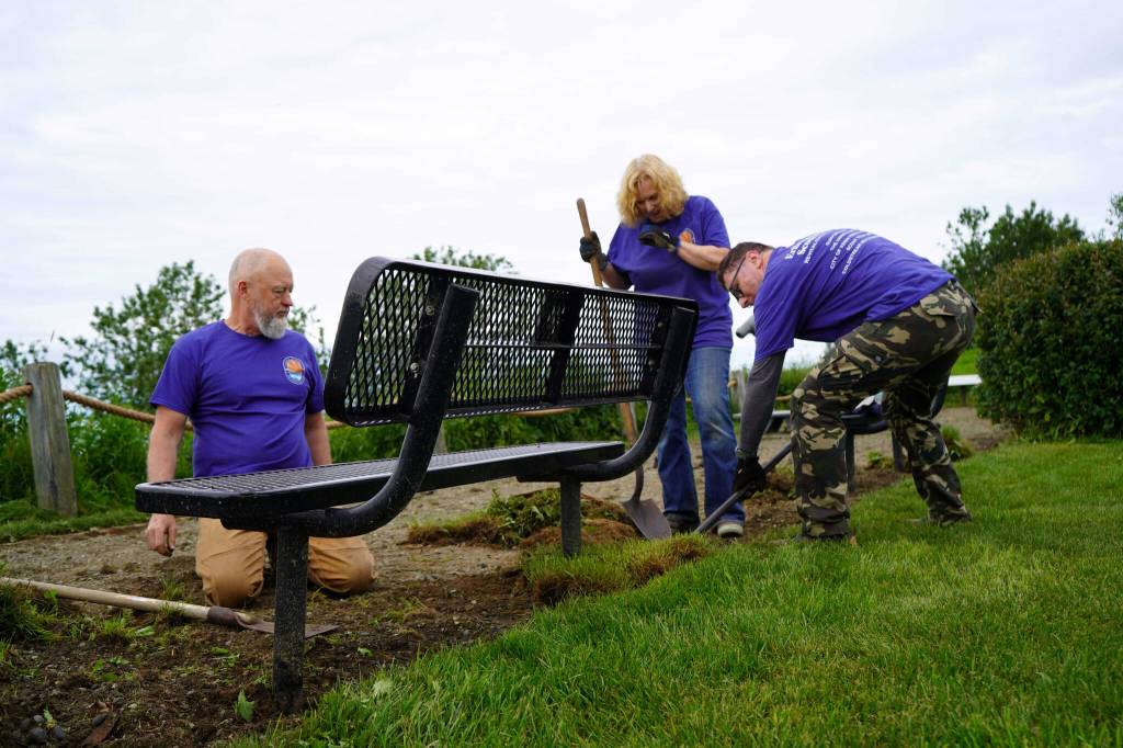 Volunteers clean around benches at Erik Hansen Scout Park in Kenai, Alaska, on Wednesday, June 25, 2025. (Jake Dye/Peninsula Clarion)